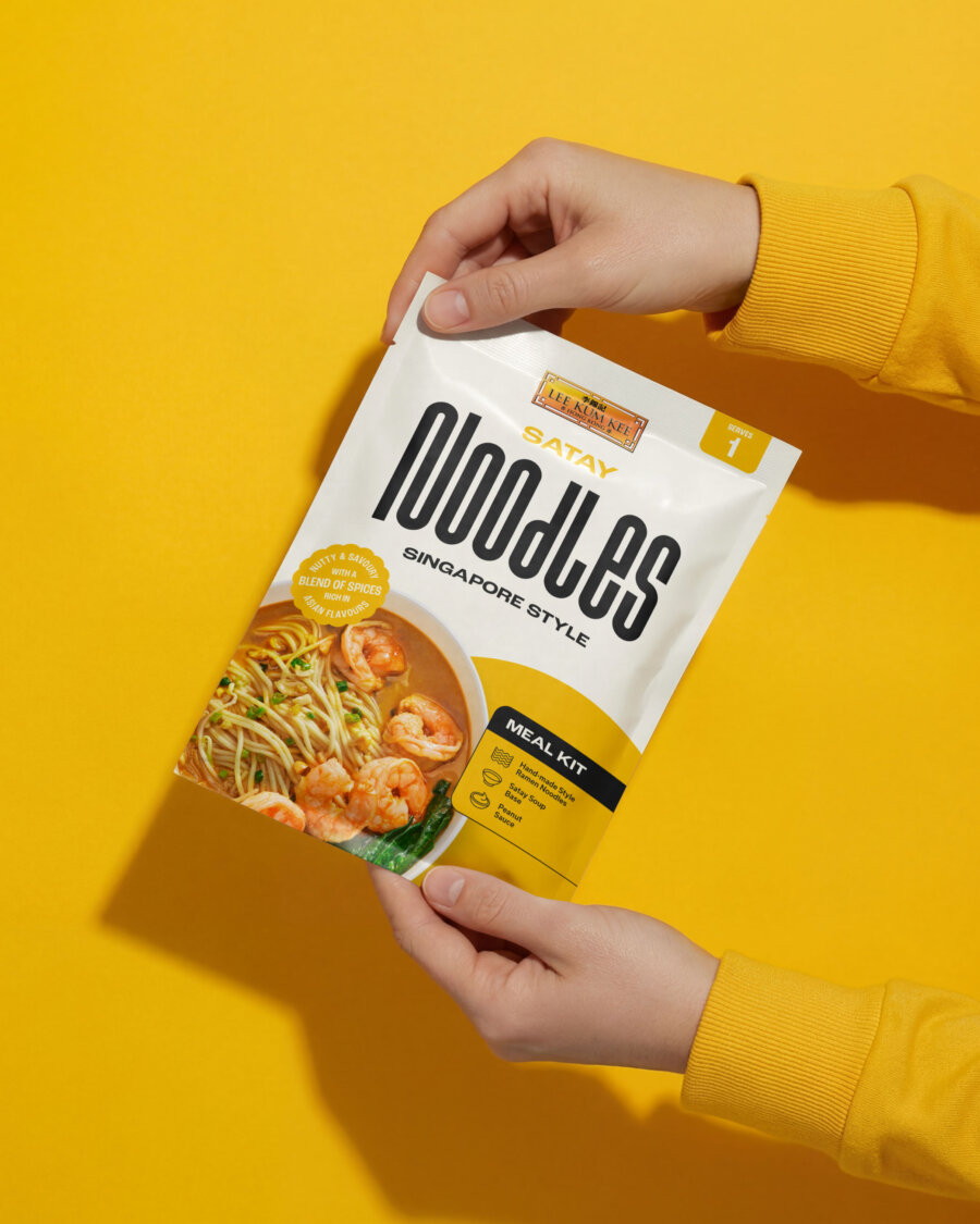 Lee Kum Kee Satay Noodles Singapore Style meal kit packet being held against a yellow background | Brand & Packaging Design by Deuce Studio London