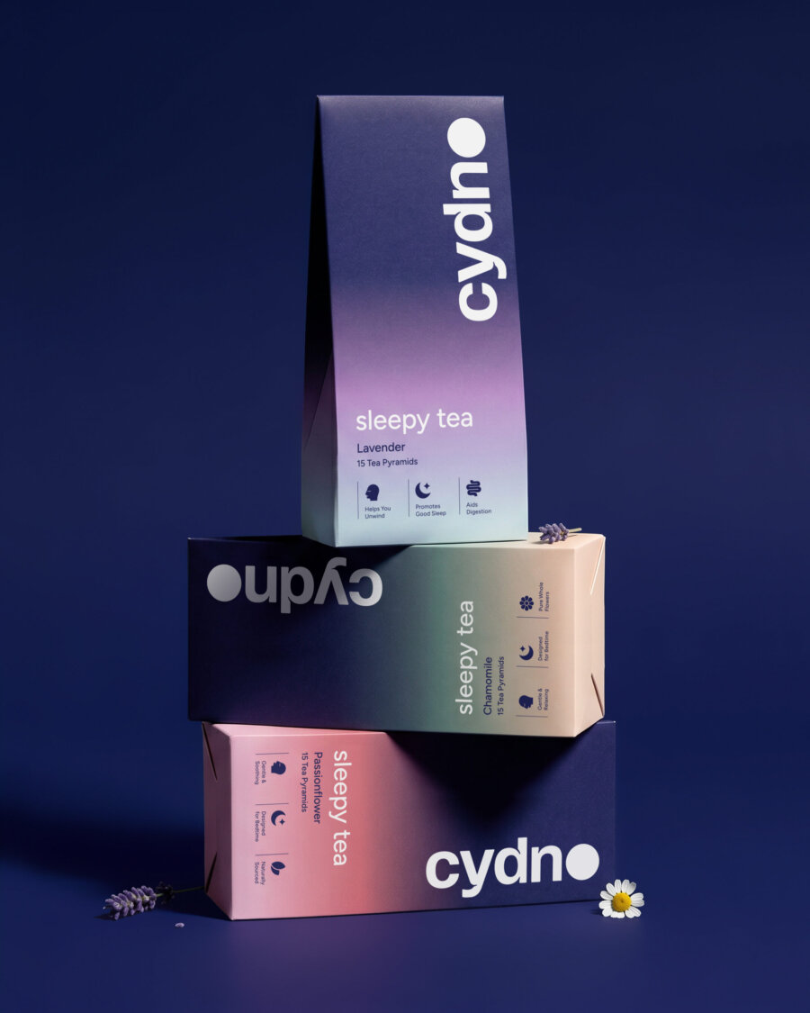 Three Cydno cartons stacked on navy with a lavender sprig and a chamomile flower