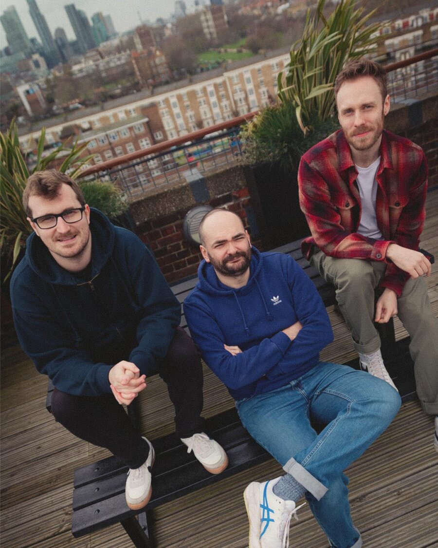 The three co-founders of Deuce Studio sitting on a bench on the studio's rooftop terrace overlooking London