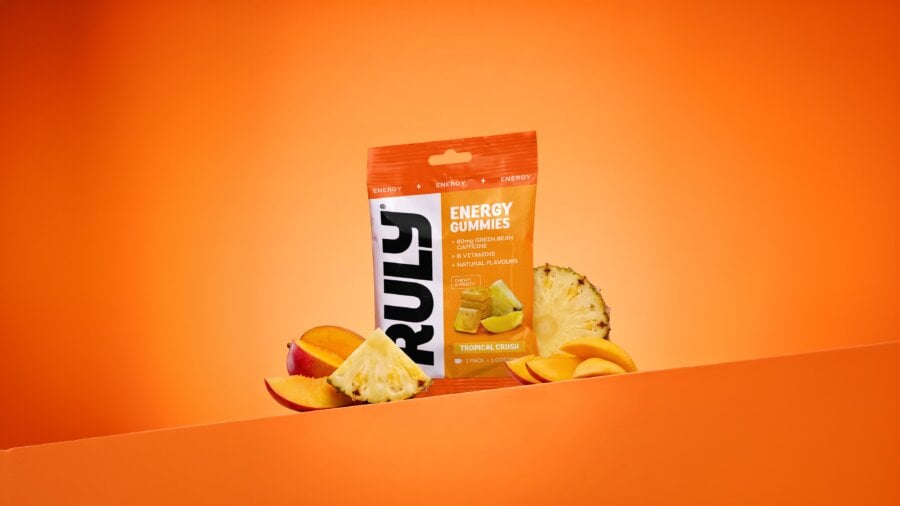 Ruly Tropical Crush energy gummies pack on an orange ledge with slices of mango and pineapple – sports nutrition branding and packaging design | Deuce Studio London